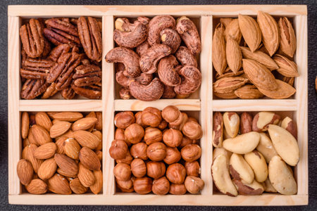 Wooden box with set of different nuts cashew, hazelnut, almond, brazil, pecan, walnut on dark concrete backgroundの写真素材