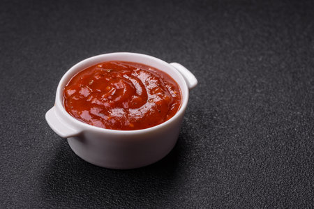 Red sauce or ketchup with salt and spices in ceramic sauce boat on dark concrete background