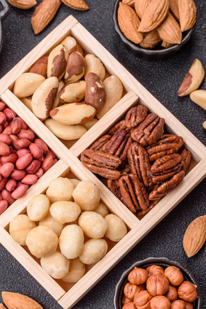 Wooden box with macadamia nuts, Brazil nuts, pecans and peanuts on a dark concrete background