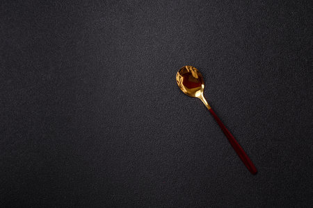 Steel spoon or teaspoon with red handle on dark concrete background. Spoon as part of kitchen utensilsの写真素材