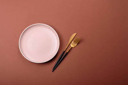 Empty ceramic plate on a monochrome brown background. Empty plate with cutlery on a dining tableの写真素材