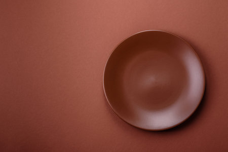 Empty ceramic plate on a monochrome brown background. Empty plate with cutlery on a dining table