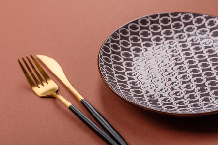 Empty ceramic plate on a monochrome brown background. Empty plate with cutlery on a dining tableの写真素材