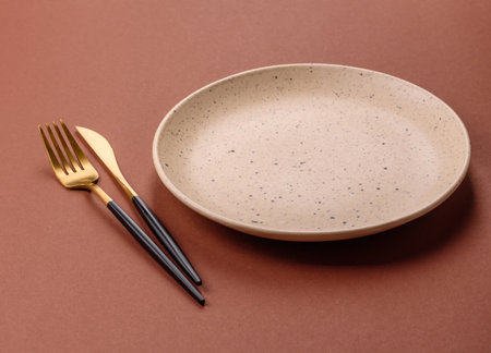 Empty ceramic plate on a monochrome brown background. Empty plate with cutlery on a dining tableの写真素材