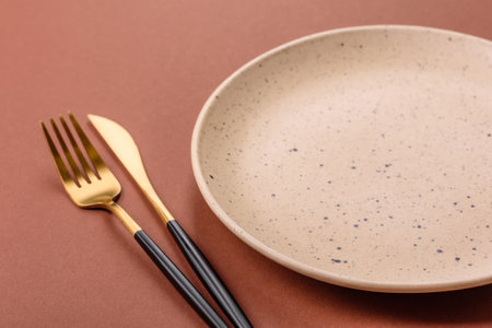 Empty ceramic plate on a monochrome brown background. Empty plate with cutlery on a dining table