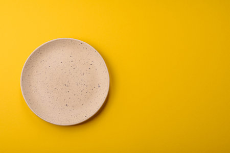 Empty round ceramic plate on yellow background. Food background for your designの写真素材