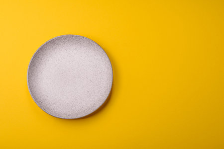 Empty round ceramic plate on yellow background. Food background for your designの写真素材