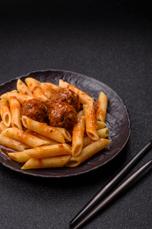 Penne pasta with meatballs in tomato sauce with salt and spices. Italian food penne pasta on dark concrete backgroundの写真素材
