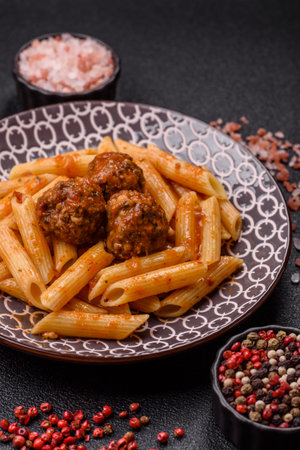 Penne pasta with meatballs in tomato sauce with salt and spices. Italian food penne pasta on dark concrete backgroundの写真素材