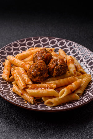 Penne pasta with meatballs in tomato sauce with salt and spices. Italian food penne pasta on dark concrete backgroundの写真素材