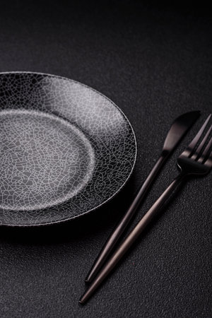 Empty round black plate for food, kitchen utensils on dining table. Empty plate on dark background