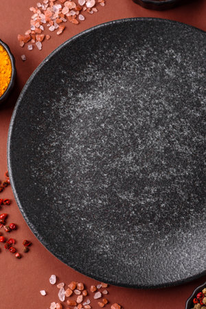 Empty round black plate for food, kitchen utensils on dining table. Empty plate on dark background