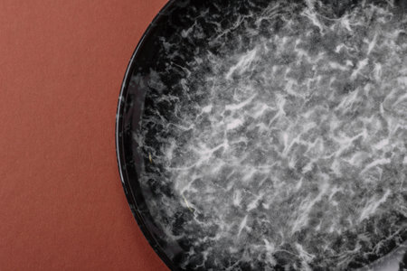 Empty round black plate for food, kitchen utensils on dining table. Empty plate on dark background