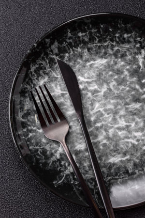 Empty round black plate for food, kitchen utensils on dining table. Empty plate on dark background