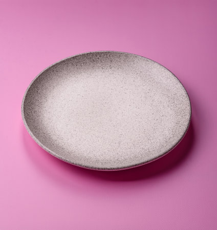 An empty round ceramic plate on a pink background as a kitchen utensil. An empty plate as a food...