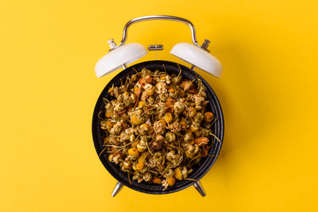 Dried chamomile flowers, herbal tea in a bowl for a hot morning drink. Dried chamomile as a plate concept instead of a dial on a vintage alarm clockの写真素材