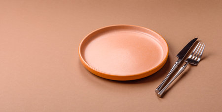 An empty round ceramic plate, knife, and fork as a dining table setting. An empty plate as a backdrop for your designの写真素材
