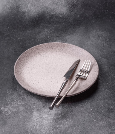 An empty round ceramic plate, knife, and fork as a dining table setting. An empty plate as a...