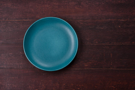 An empty round ceramic plate on a dark, textured brown background. An empty round plate as a food background for your design