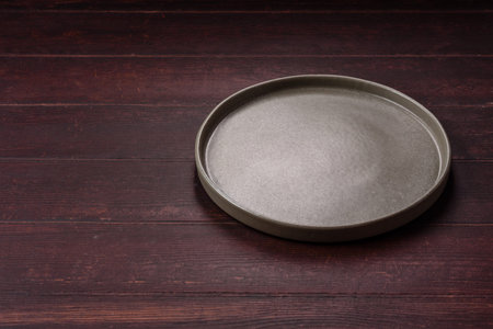 An empty round ceramic plate on a dark, textured brown background. An empty round plate as a food background for your design