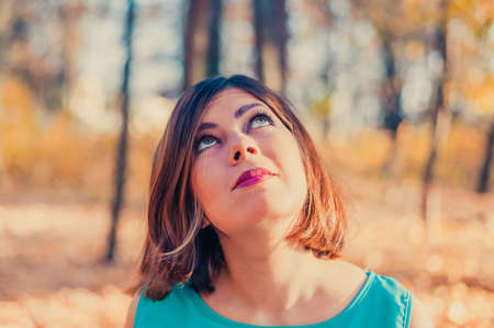 pretty red-haired teen girl in blue clothes looks up in the autumn park