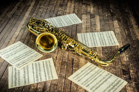 beautiful yellow saxophone and paper with music score notes lying on a vintage wooden stageの写真素材