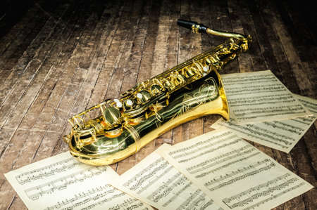 shiny golden saxophone lies near sheet music letters on a wooden stageの写真素材