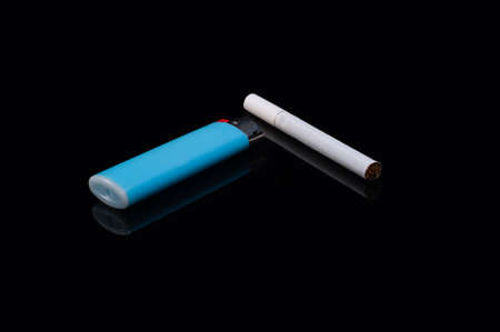 one white filter cigarette and a plastic gas blue lighter on an isolated black background with reflectionの写真素材
