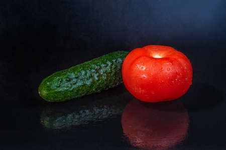 fresh vegetables - green cucumber and red tomato on an isolated black background with reflectionの写真素材