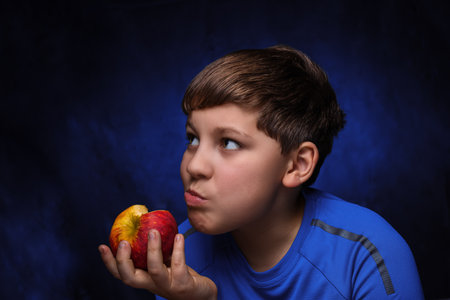 big red-yellow apple in the hand of eating it European teenage boy with light brown hair, dressed in...