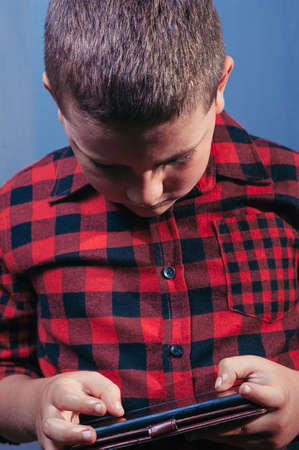 white teenage boy with light brown hair wearing red plaid shirt playing on smartphoneの写真素材