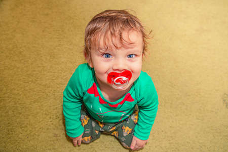cheerful smiling red-haired baby boy sits on the floor with a pacifier in his mouthの写真素材