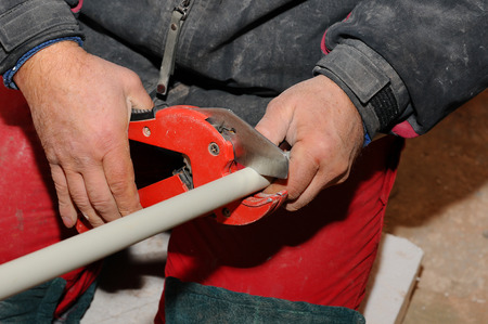 Plumber worker with scissors cuts the tube. cutting metal-plastic pipe by special red scissors. Plumber hands working with grey pipe on blurred background. plumbing pipes. individual heating system.の写真素材