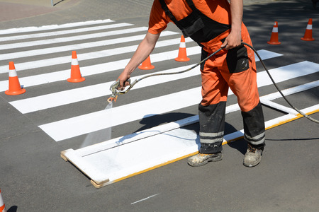Worker is painting a pedestrian crosswalk. Technical road man worker painting and remarking pedestrian crossing lines on asphalt surface using paint sprayer gun.の写真素材