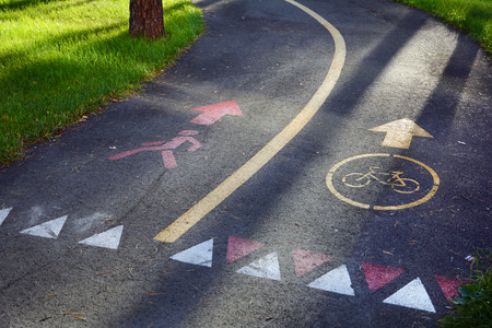 The sidewalk and bike path. Yellow bicycle sign on asphalt bike lane on city park in background.の写真素材