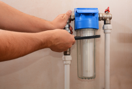 The plumber installs a new cartridge for the water filter. Filter system for water treatment. Installation of a reducer and a water filter for water purification.の写真素材