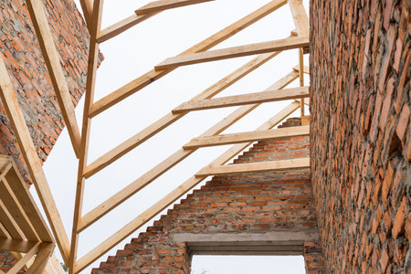 Installation of wooden beams at construction the roof truss system of the brick house.