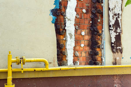 Closeup part of the building gas pipe damaged after shelling. A burnt facade and a visible brick...