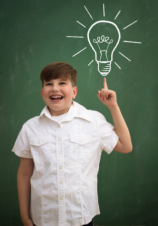 happy smart child in class against blackboard with drawing light bulb idea. Education conceptの写真素材