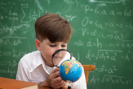 Schoolboy looking through a magnifying glass at the globeの写真素材