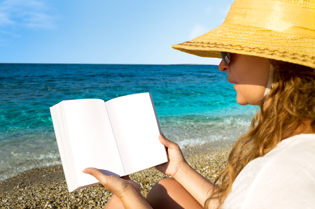 Curly hair female reading a book on the beach.の写真素材