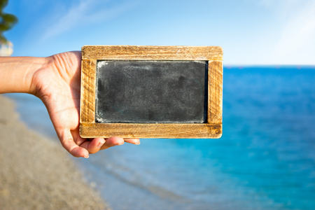 Female hand holding empty blackboard over beautiful sea shoreの写真素材