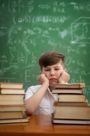 tired and bored schoolboy sitting at a table with books, emotion expressionの写真素材