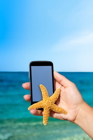 phone with isolated screen in hand with starfish at the beach in backgroundの写真素材