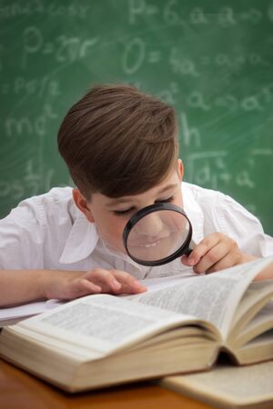 education and school concept - little student boy reading book with magnifier at schoolの写真素材