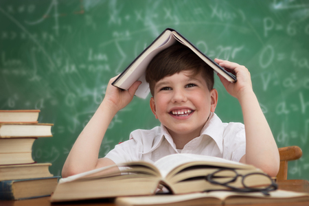 Happy little boy, pupil with book on head, education conceptの写真素材