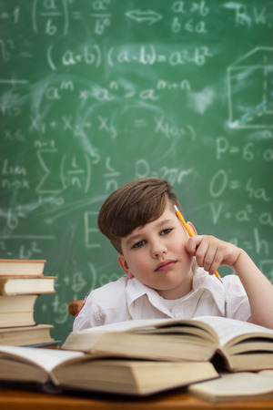 Thinking schoolboy sitting at desk with bookの写真素材