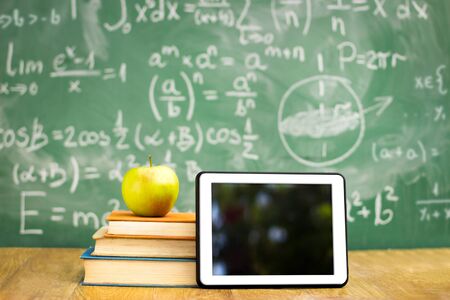 Digital tablet and apple on the desk in front of blackboard