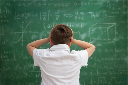 Schoolboy holding hands on his head,  getting crazy and looks at the blackboard with formulasの写真素材