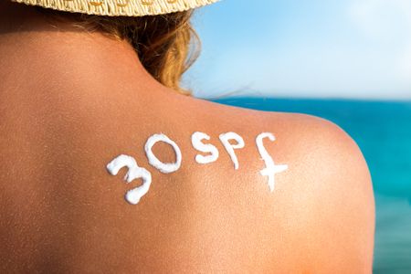 skin care and sun protection, woman with sunscreen lotion on back at the sea shoreの写真素材